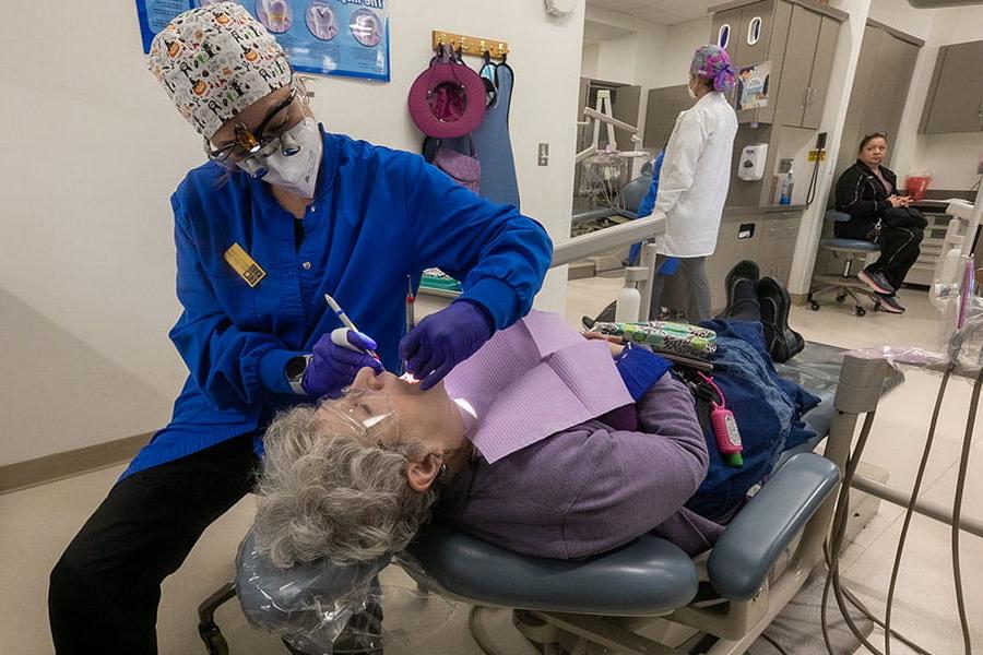 一名学生卫生员正在检查一位躺在牙科椅上的妇女的口腔